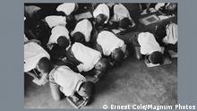 Schwarze Kinder knien in einer südafrikanischen Schule während der Apartheid zum Schreiben auf dem Boden.