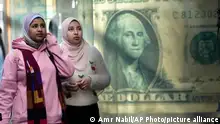 Egyptians walk past a poster depicting a U.S. dollar outside an exchange office in Cairo, Egypt, Thursday, Feb. 9, 2023. Egypt continues to battle surging inflation amid a dramatic slide of its currency as many Egyptians struggle with price hikes, the country's statistics bureau said. (AP Photo/Amr Nabil)