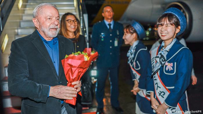 Luis Inácio Lula da Silva con un ramo de flores al bajar las escalinatas del avión junto a dos sonrientes azafatas japonesas.