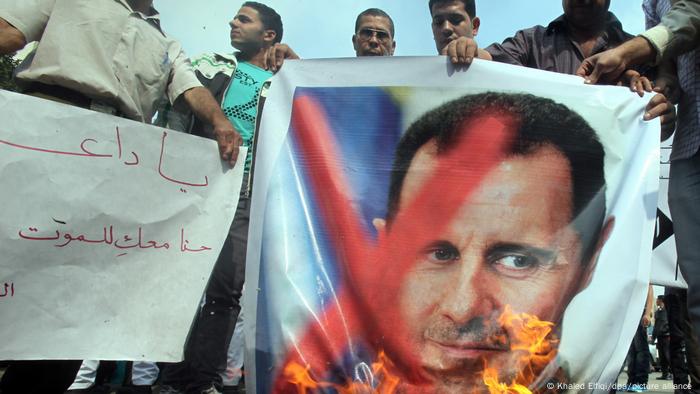 Demonstranten verbrennen ein Bild Assads mit einem roten Kreuz