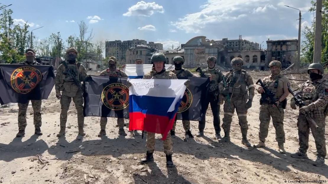 Prigozhin segura uma bandeira russa em frente a um grupo de oito soldados