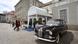 Guests enter the church building, with a BMW 505 Pullman Limousine, the wedding car, parked outside awaiting the couple
