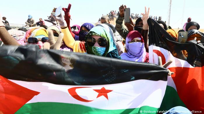 Mujeres vestidas con el traje saharaui tradicional sostienen banderas del Sáhara Occidental y levantan los brazos en señal de victoria.
