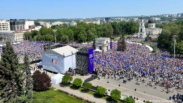 Demonstration mit vielen EU-blauen Flaggen vor einer großen Bühne gegenüber einer Kirche aus der Vogelperspektive