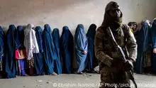 A Taliban fighter stands guard as women wait to receive food rations distributed by a humanitarian aid group, in Kabul, Afghanistan, Tuesday, May 23, 2023. (AP Photo/Ebrahim Noroozi)