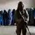 A Taliban fighter stands guard as women wait to receive food rations distributed by a humanitarian aid group, in Kabul,