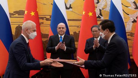 Die Ministerpräsidenten Russlands und Chinas, Michail Mischustin (l) und Li Qiang (r) vor russischen und chinesischen Flaggen und zwei applaudierenden Männern