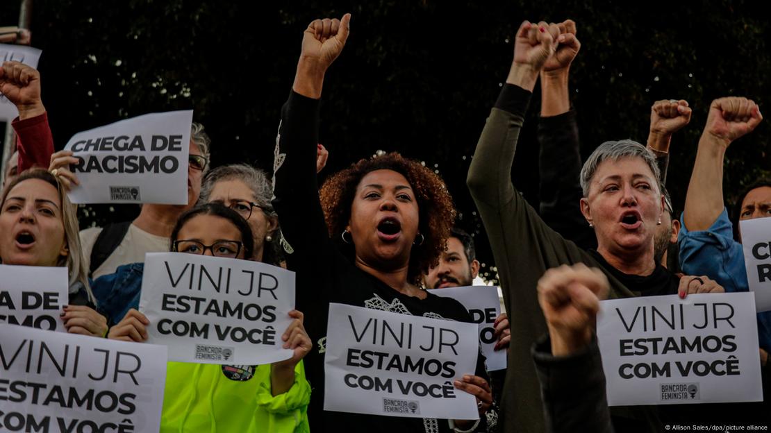 Em protesto contra os ataques racistas ao jogador brasileiro do Real Madrid, Vinicius Junior, manifestantes de punhos erguidos seguram cartazes com os dizeres: Em protesto contra os ataques racistas ao jogador brasileiro do Real Madrid, Vinicius Junior, manifestantes de punhos erguidos seguram cartazes com os dizeres: