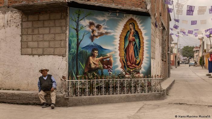 Un hombre sentado en la acerca junto a un mural de la Virgen de Guadalupe, en México. Un hombre sentado en la acerca junto a un mural de la Virgen de Guadalupe, en México.