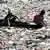 Two men in a small wooden boat float through plastic waste in a polluted river