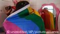 Mann aus Uganda im Profil, eingehüllt in Regenbogenfahne, die Oberkörper und Gesicht bedeckt