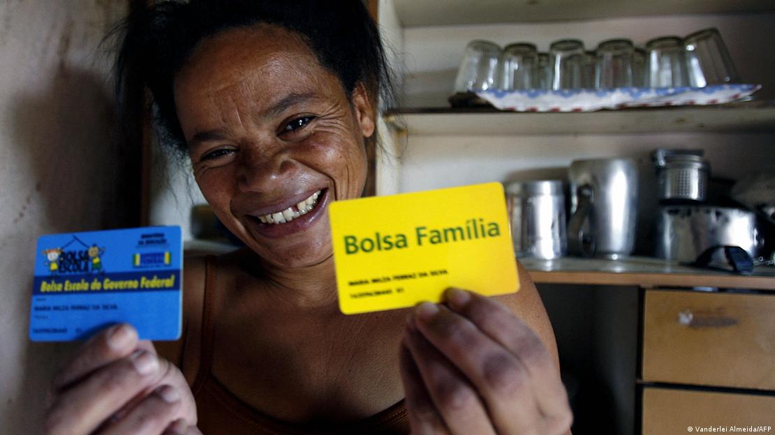 Brasileiroa segura um cartão do Bolsa Família e um cartão do Bolsa Escola 