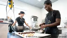 Rebecca Biira (r), Hospitantin aus Uganda, steht in der Bäckerei Wippler und überzieht Pralinen mit flüssiger Schokolade. Die berufliche Auslandserfahrung ist Teil eines Projektes zur Fachkräfteförderung des Deutsch-Afrikanischen Jugendwerkes (DAJW), welches junge Fachkräfte aus Deutschland nach Afrika bringt und umgekehrt.