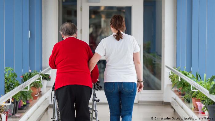 A nurse accompanies an elderly woman with a walker