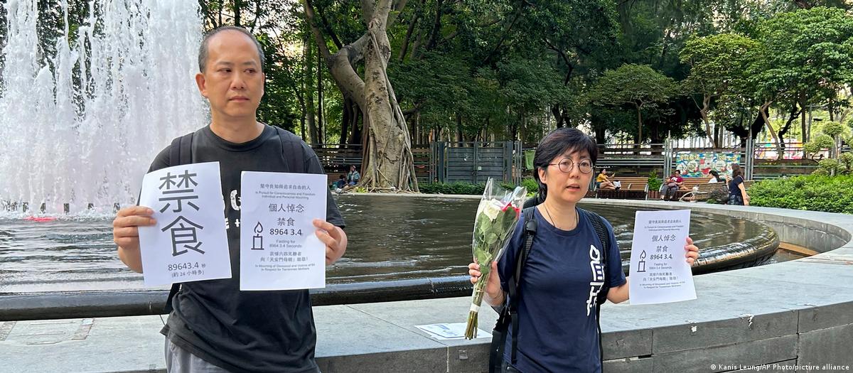 Activists Kwan Chun-pong, left and Lau Ka-yee at right hold up papers at the entrance to Hong Kong's Victoria Park on June 3, 2023