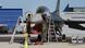 Dos operarios militares revisan los sistemas de vuelo de la aeronave frente a un hangar. Dos operarios militares revisan los sistemas de vuelo de la aeronave frente a un hangar.