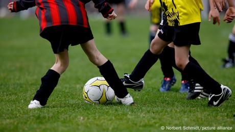 Junge Spieler mit unterschiedlichen Trikots spielen auf einem Rasen Fußball. (Quelle: Norbert Schmidt/picture alliance)