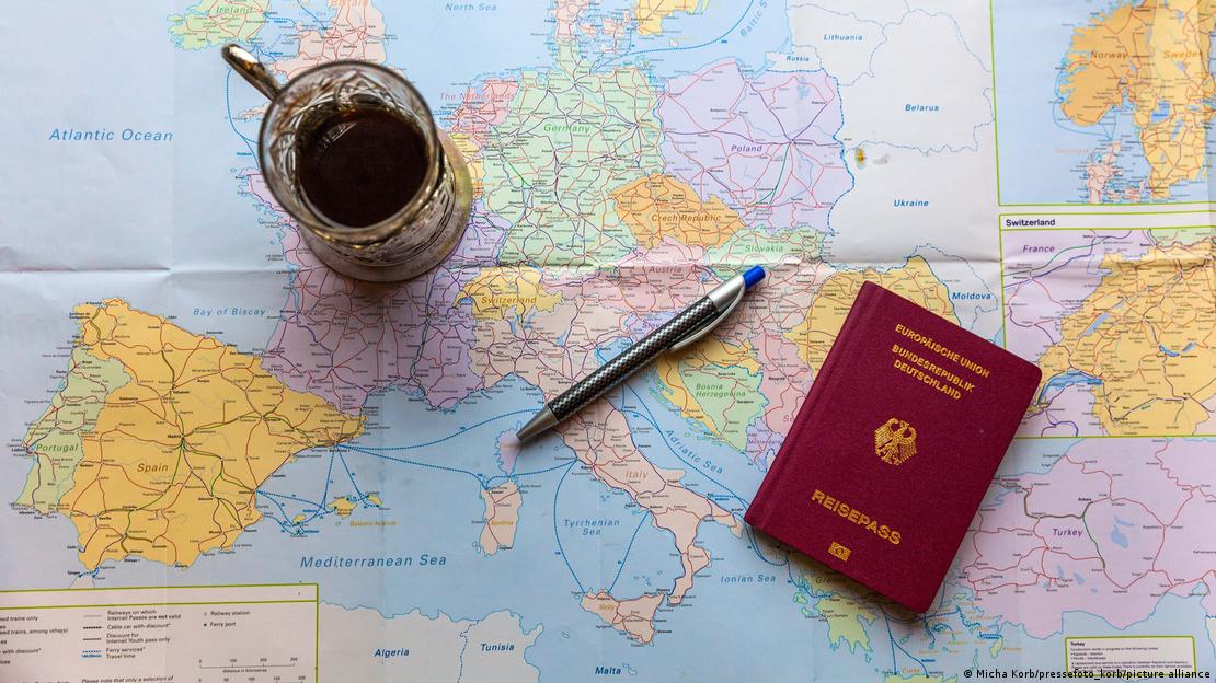 Una imagen de un mapa de Europa y un pasaporte alemán, junto a una taza de café. 
