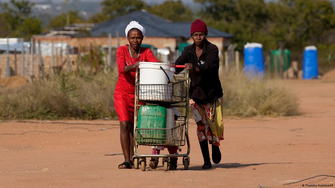 Two people pushing buckets filled with treated water on a shopping trolley along a dusty road Two people pushing buckets filled with treated water on a shopping trolley along a dusty road