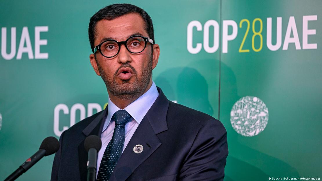 Sultan Ahmed al-Jaber fala ao microfone em frente a um fundo verde com a dizer COP28UAE