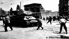 People throwing stones at a tank in the middle of an East Berlin street