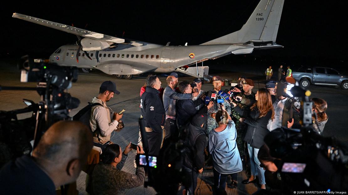 Militar de roupa camuflada concede entrevista em frente a um avião