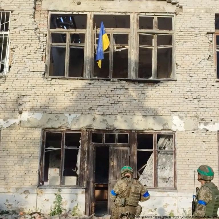 Un hombre con uniforme militar se para en un edificio destruido.