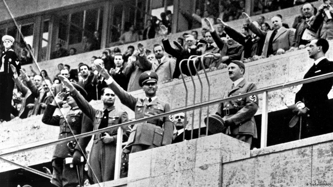 Ceremonia inaugural de 1936: Adolf Hitler en el Estadio Olímpico. Todos a su alrededor hacen el saludo nazi, alzando la mano derecha. 