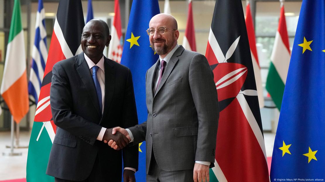 William Ruto shakes hands with Charles Michel as they stand in front of numerous flags