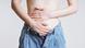 Frau in Jeans, die sich mit beiden Händen den Bauch hält Frau in Jeans, die sich mit beiden Händen den Bauch hält