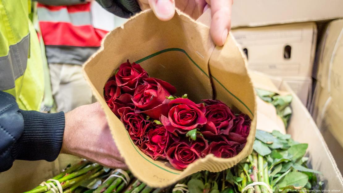 A man holds up a bag of red roses from a carton full of the flowers