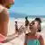 Mutter cremt Tochter am Strand mit Sonnencreme ein