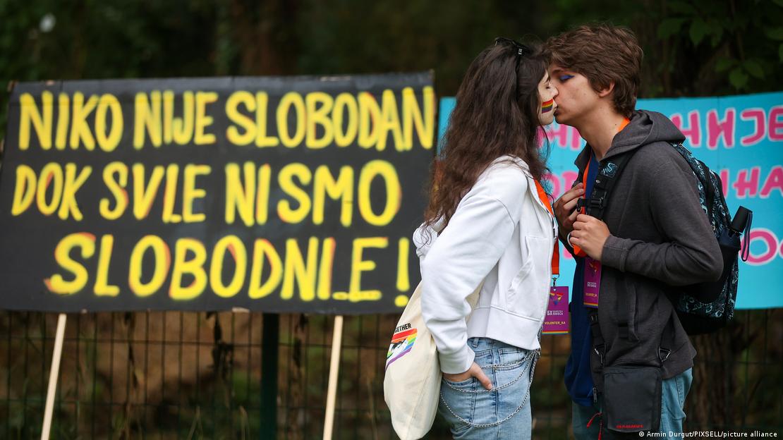 Parada ponosa u Sarajevu 24.6.2023: Dvoje mladih se ljube a iza njih je transparent: "Niko nije slobodan dok svi nismo slobodni/e!"