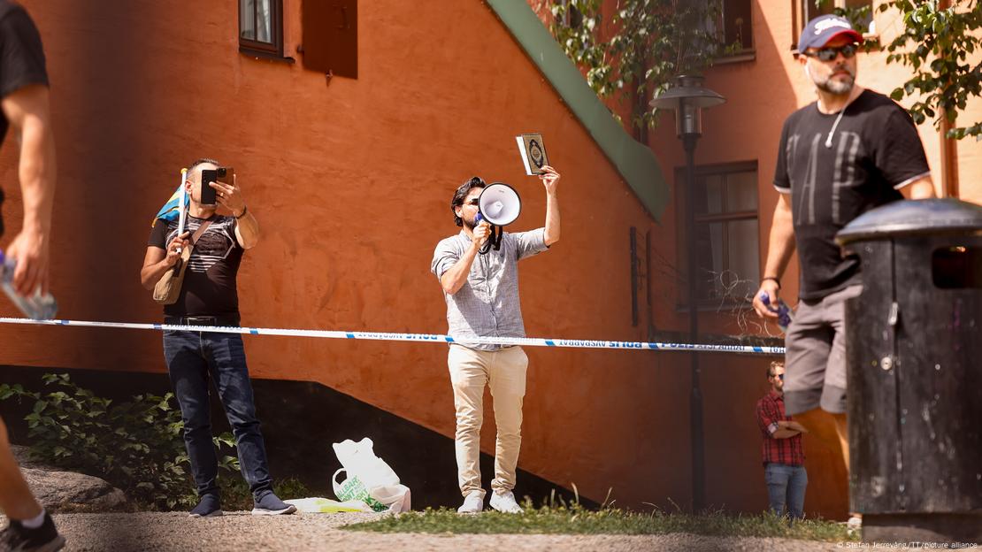 A man stands with a megaphone, holding aloft a copy of the Quran, outside a mosque in Stockholm. He would later set some pages from the book on fire. June 28, 2023. 