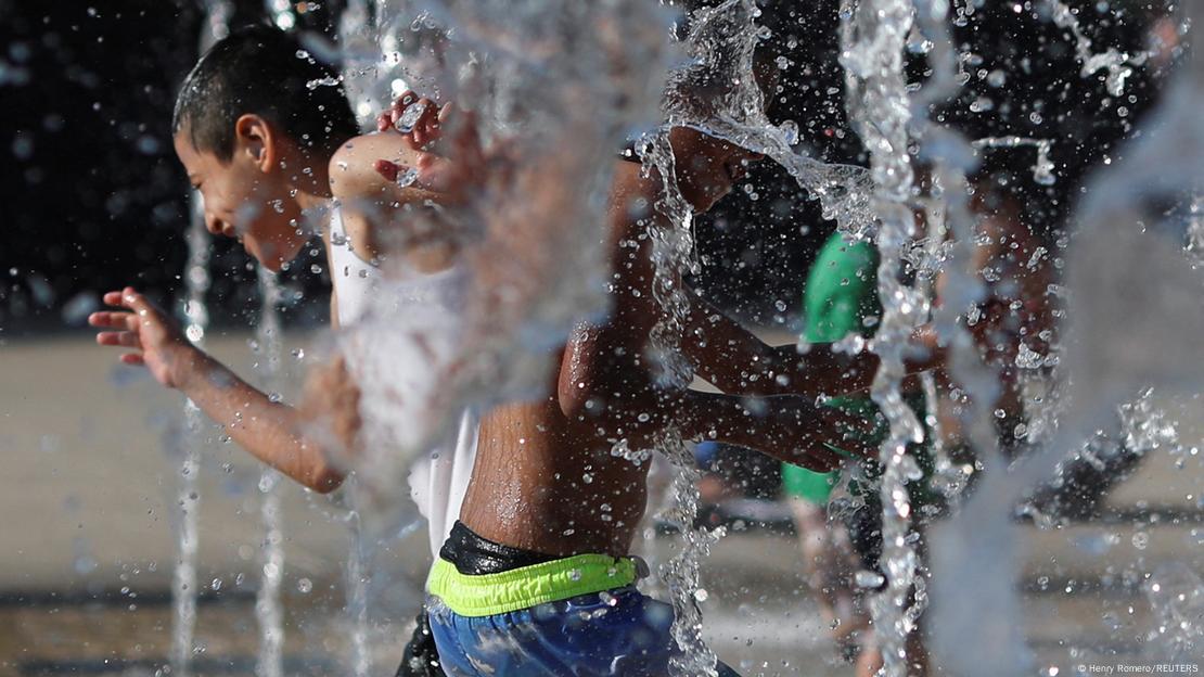 Un joven se refresca jugando en una fuente.