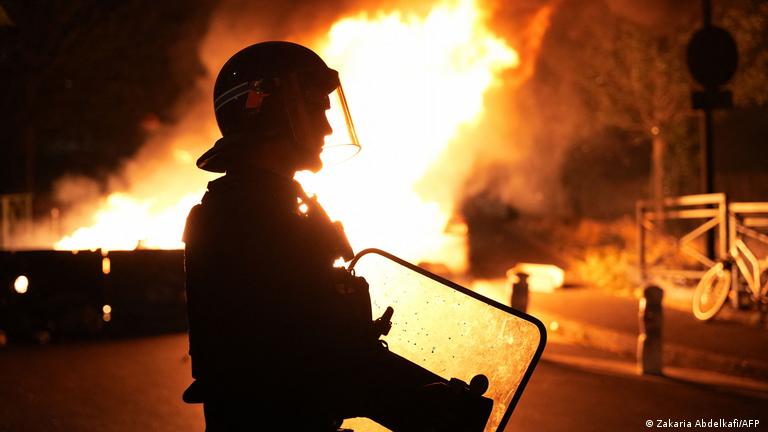 Protestas en Francia: un policía con un escudo, cerca de incendios en la calle.