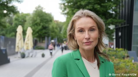 A cientista política Margarita Šešelgytė aparece de blazer verde, olhando para a câmera, em uma rua de Vilnius, capital da Lituânia.