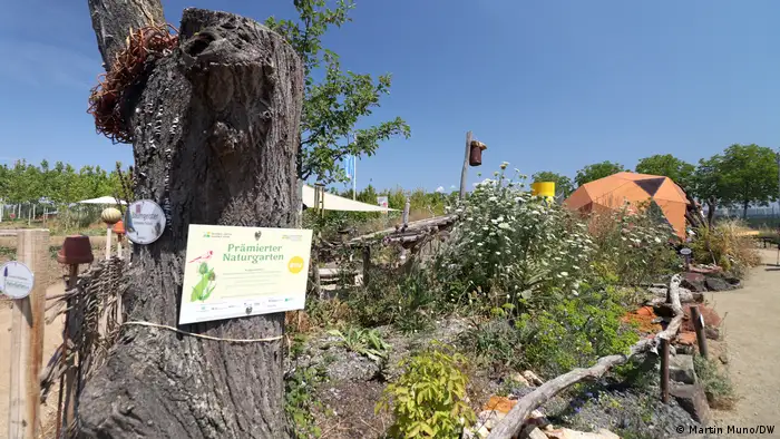 Ein Schild Prämierter Naturgarten auf einem abgestorbenen Baum vor einem Garten