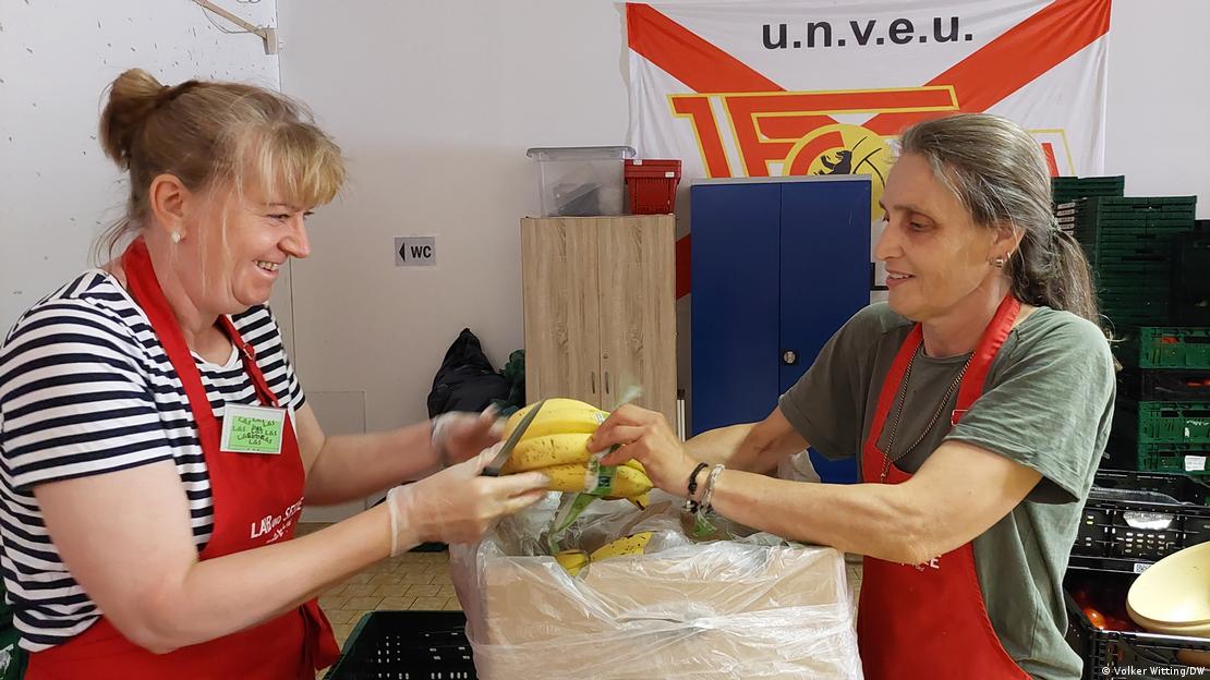 Zwei Frauen mit Bananen in ihren Händen, die aus einer Schachtel extrahiert werden, tragen rote Tabletts mit Bananen in ihren Händen, die aus einer Schachtel genommen wurden und rote Tabletts tragen