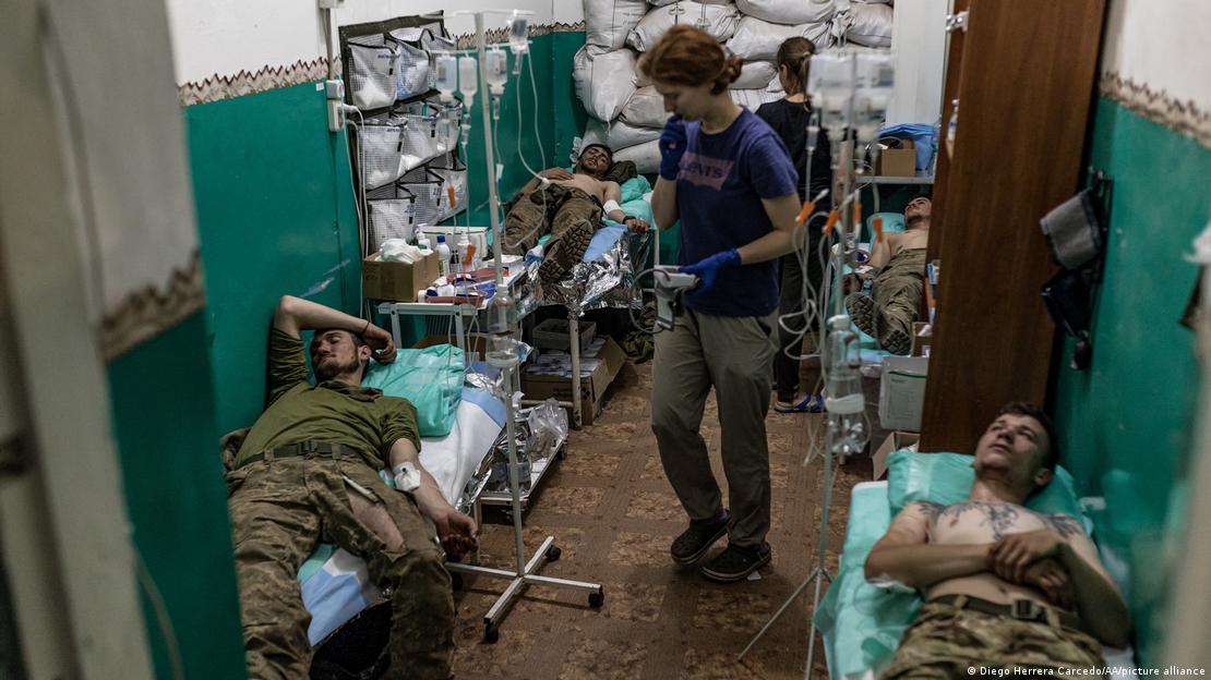 Ranjeni muškarci u uniformama leže u hodniku na bolničkim krevetima
