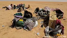 Migrants from sub-Saharan African countries who claim to have been abandoned in the desert by Tunisian authorities without water or shelter, sit in an uninhabited area near Libya's border town of Al-Assah on July 16, 2023. Hundreds of migrants from sub-Saharan African countries were forcibly taken to desert and hostile areas bordering Libya and Algeria after unrest in early July in Sfax, Tunisia's second-largest city. (Photo by Mahmud Turkia / AFP)