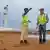 Two construction workers stand on a sandy site with puddles around them
