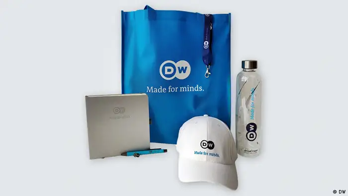 Verschiedene Produkte mit dem Logo der DW: ein Kappe, eine Trinkflasche, eine Tasche und ein Schreibheft mit Kugelschreiber