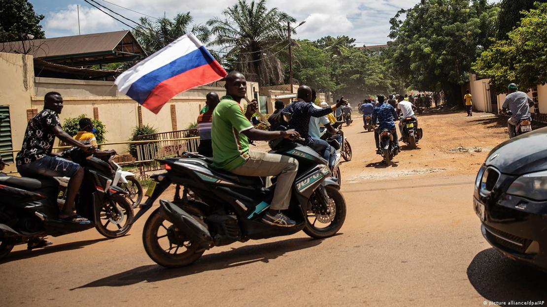 Homem de moto dirige enquanto segura uma bandeira da Rússia