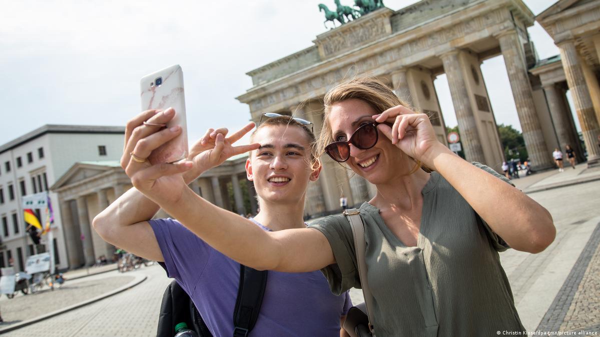 A man and woman pose for a selfie in front of the Brandenburg Gate.