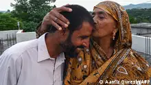 In this picture taken on July 17, 2023, Pakistani worker Muhammad Naeem Butt (L) is kissed by his mother Razia Latif at their home in Khuiratta. After spending weeks in Libya trying to reach Europe illegally, Butt turned back -- abandoning a journey that has already cost hundreds of Pakistani lives this summer. Shovelling sand onto a truck surrounded by Pakistan's Kashmir valley, he says he ended his treacherous bid for a better life when an overloaded fishing trawler sank off the coast of Greece last month. (Photo by Aamir QURESHI / AFP) / To go with 'Pakistan-Migration', FOCUS by Zain Zaman JANJUA and Sajjad QAYYUM