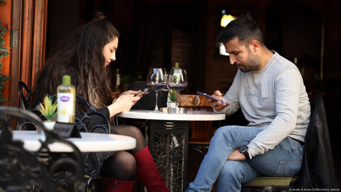 A man and a woman sit outside a coffee shop looking at their phones A man and a woman sit outside a coffee shop looking at their phones