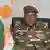 Militar con gafas y una bandera de fondo da un discurso por televisión. 