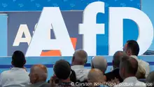 Delegierte sitzen vor dem Parteilogo bei dem AfD-Bundesparteitag in der Magdeburger Messe hoch.