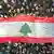 A crowd holds a large Lebanese flag above them with writing on it
